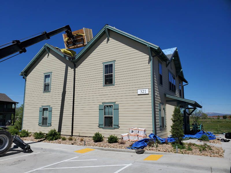 Custom Exteriors loading roofing supplies on building during multi-family roof replacement