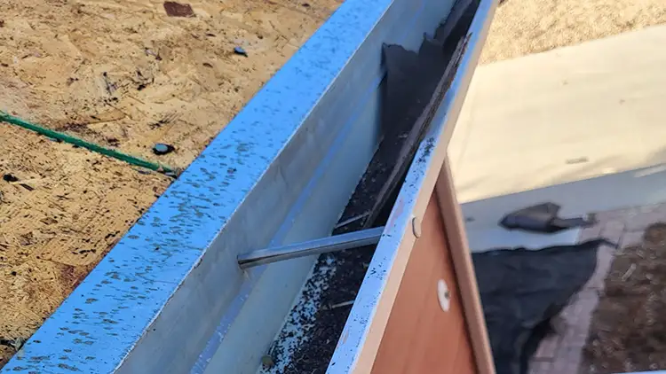Apron flashing - Custom Exteriors, LLC Close-up of a blue metal edge trim on a construction site, with a metal rod protruding inside a frame.